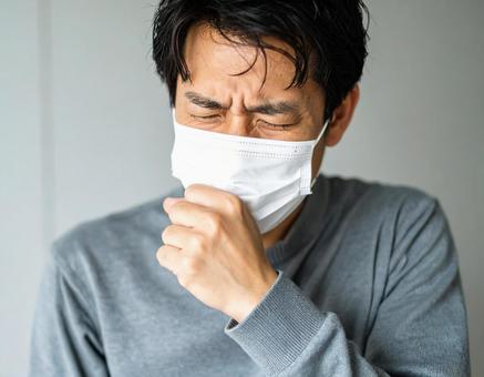 マスクを着用して咳をするの男性の写真