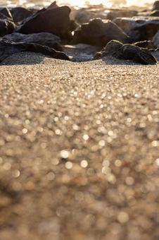 朝日に輝く砂浜と岩_縦の写真