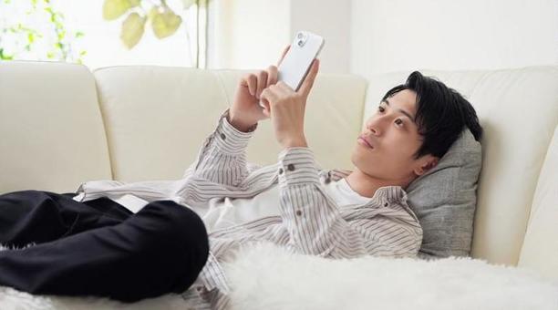 寝ながらスマホを見るアジア人男性 寝ながらスマホを見るアジア人男性 スマホ,スマートフォン,男性の写真素材