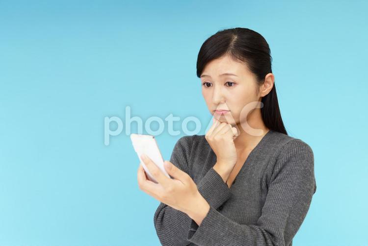 スマートフォンを持つ不安そうな表情の女性 女性,スマートフォン,携帯電話の写真素材