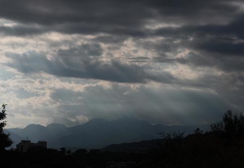雲間から日が差す山並みの写真