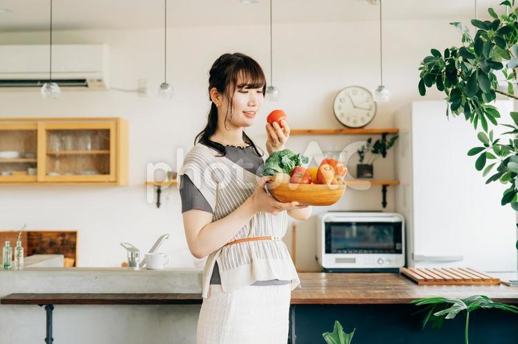 キッチンの前に野菜を持つ女性（トマト） 野菜,トマト,女性の写真素材