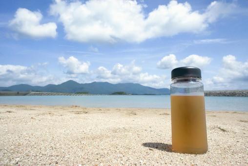 ＜素材＞夏の砂浜に置かれたお茶のボトル 夏,海,水筒の写真素材