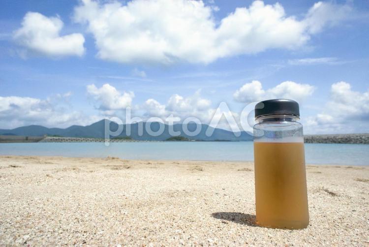 ＜素材＞夏の砂浜に置かれたお茶のボトル 夏,海,水筒の写真素材