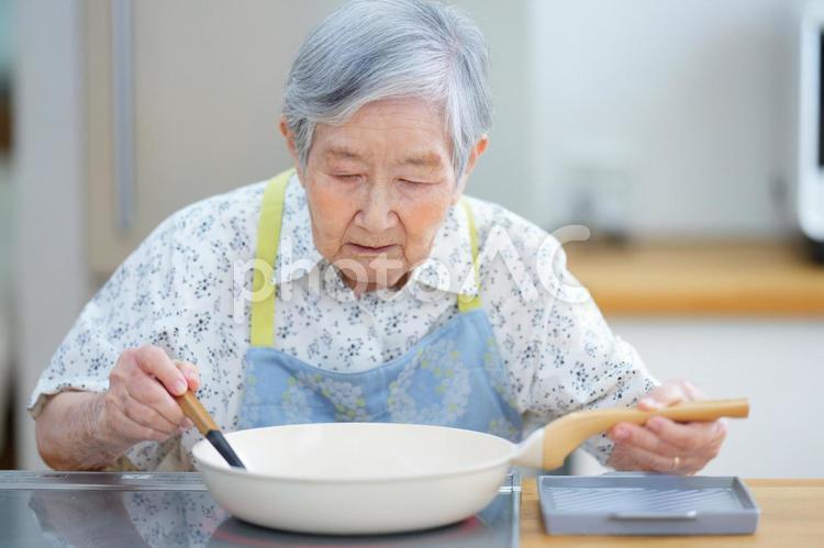 白いフライパンで調理中の高齢女性 女性,料理,フライパンの写真素材