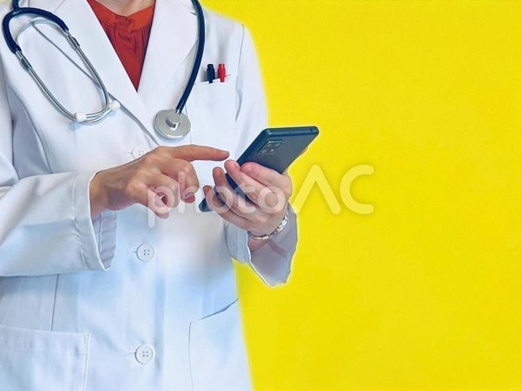 スマホを操作する女性医師（イエロー背景） スマホ,女医,操作の写真素材