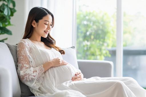 ソファに座っている若い日本人の妊婦 ソファに座っている若い日本人の妊婦の写真