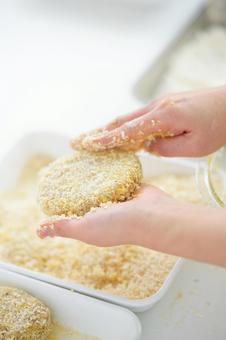 コロッケにパン粉をつけている手の写真