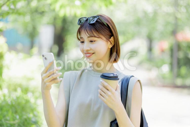 新緑の中スマートフォンを使う女子大生 女性,外出,スマートフォンの写真素材