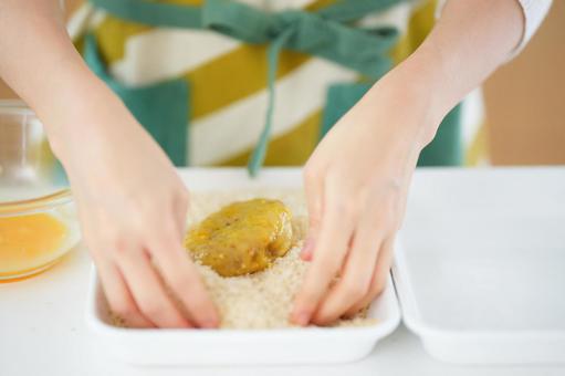 コロッケにパン粉をつけようとしている人の手 コロッケにパン粉をつけようとしている人の手の写真