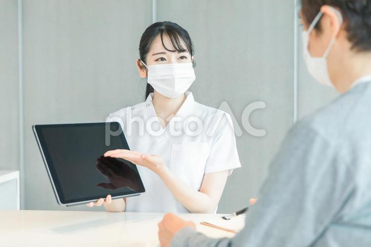 タブレットPCで受付する白衣の女性と患者 病院,受付,レセプトの写真素材