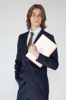 ノートパソコンを抱えてポケットに手を入れたカメラ目線のスーツの男性 男性,外国人,欧米人の写真素材