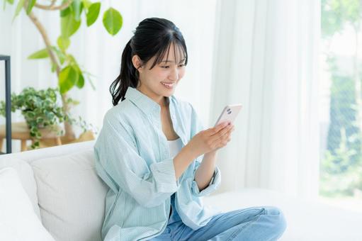 部屋でスマホを操作する若い女性 スマホ,笑顔,女性の写真素材