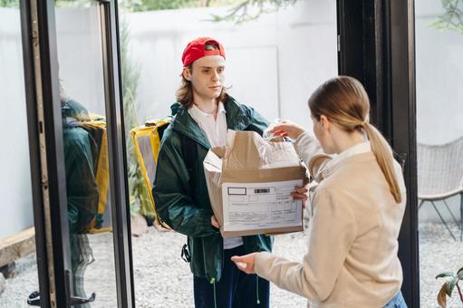 玄関で潰れた段ボール箱を受け渡す配達員の男性 配達,フードデリバリー,デリバリーの写真素材