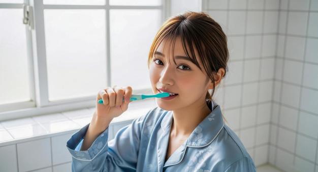 朝の洗面所で歯磨きをする若い女性 朝の洗面所で歯磨きをする若い女性の写真