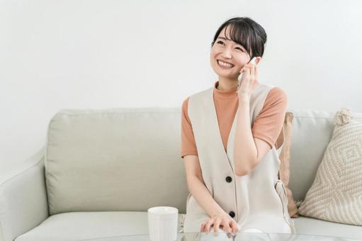 ソファに座ってスマホで電話する笑顔の女性 ソファに座ってスマホで電話する笑顔の女性 スマホ,通話,女性の写真素材