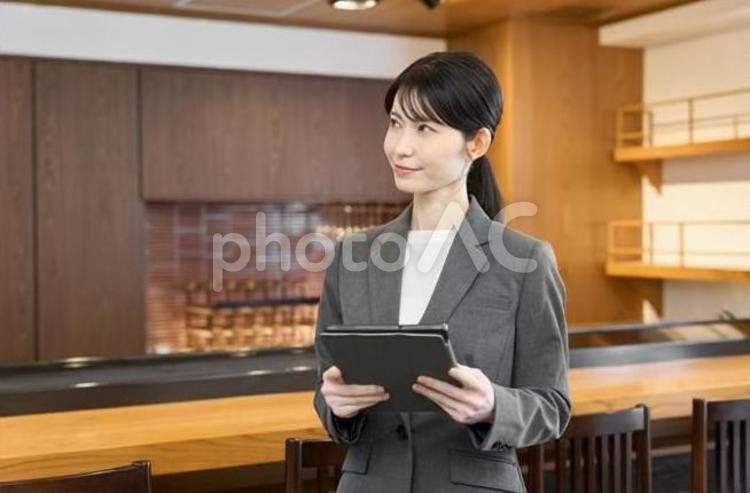 タブレットを持って店内を見る女性 飲食店,女性,スーツの写真素材