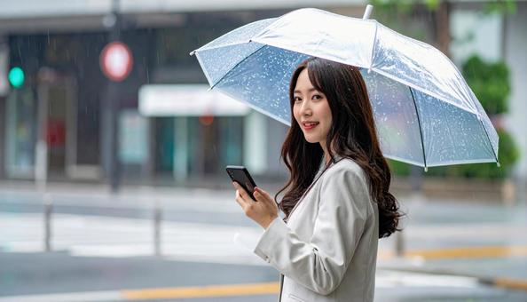 傘をさしてスマホを使う若い日本人女性 傘をさしてスマホを使う若い日本人女性の写真