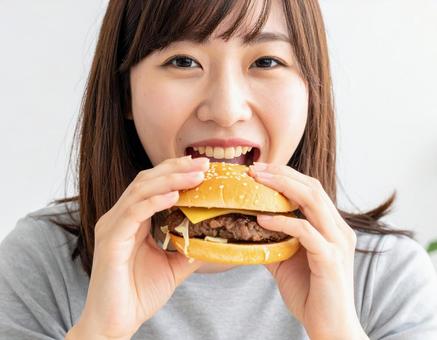おいしそうにハンバーガーにかじりつく女性の写真