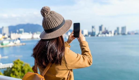 海の向こうを携帯で撮影する観光客の女性 海の向こうを携帯で撮影する観光客の女性の写真