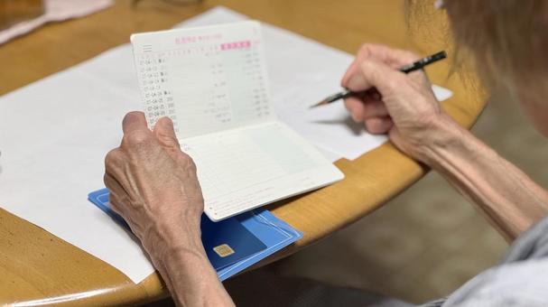 通帳を開いてメモに書き込む高齢女性の手 通帳を開いてメモに書き込む高齢女性の手 貯金通帳,預金通帳,口座の写真素材