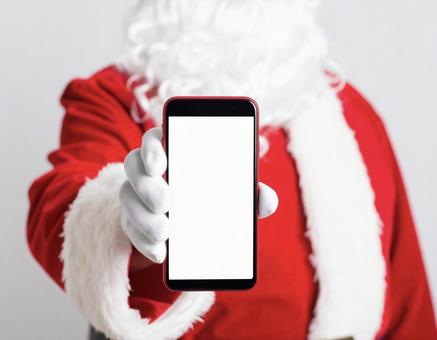 白いスマホの画面を見せるサンタクロース 白いスマホの画面を見せるサンタクロースの写真