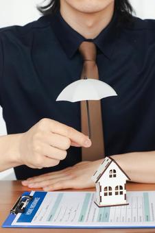 小さな傘で家の模型を守る男性スタッフの写真