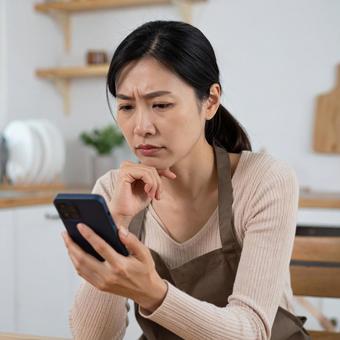 スマホを見て不安そうな表情を浮かべる女性の写真