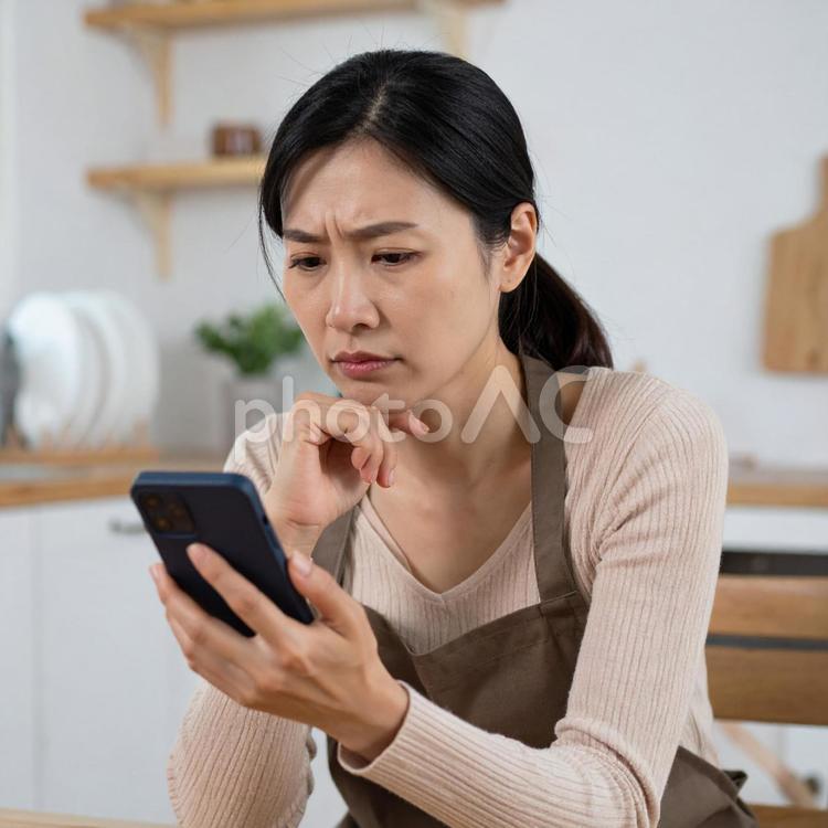 スマホを見て不安そうな表情を浮かべる女性 主婦,日本人女性,スマホの写真素材