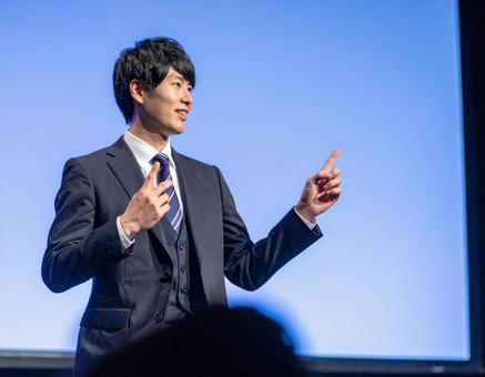 ステージ上で堂々とプレゼンする男性 ステージ上で堂々とプレゼンする男性の写真