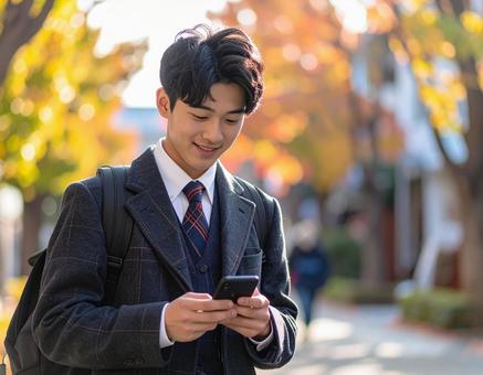 秋の公園でスマホを操作する男子高校生の写真