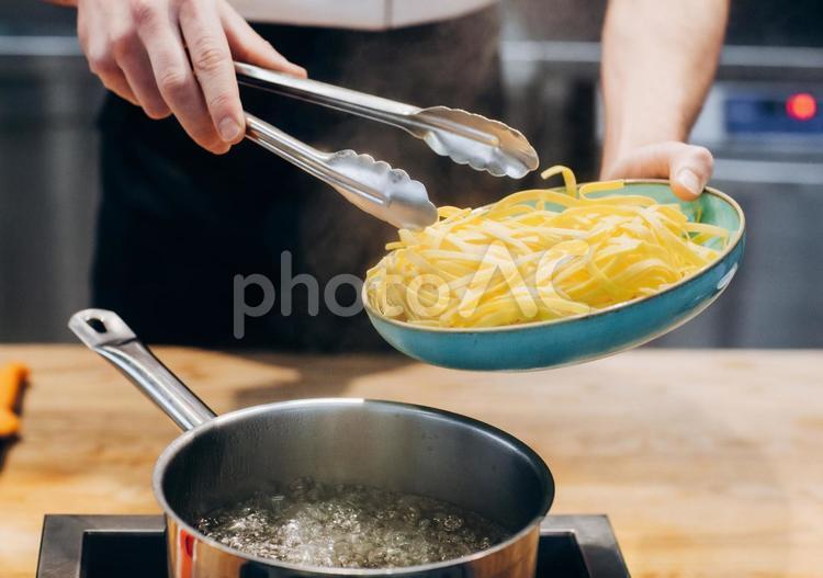 鍋に麺を入れるシェフの手元 キュイジーヌ,キッチン,厨房の写真素材