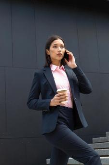 オフィスビルの外の階段でコーヒー片手に電話しているビジネスウーマン ビジネスウーマン,ビジネス,女性の写真素材