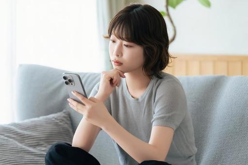 スマホを見て考えごとをする女性 スマホを見て考えごとをする女性の写真