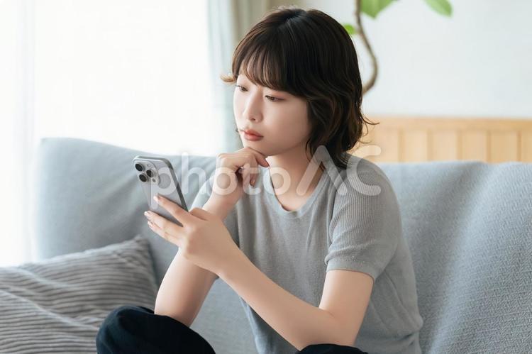 スマホを見て考えごとをする女性 女性,スマホ,スマートフォンの写真素材