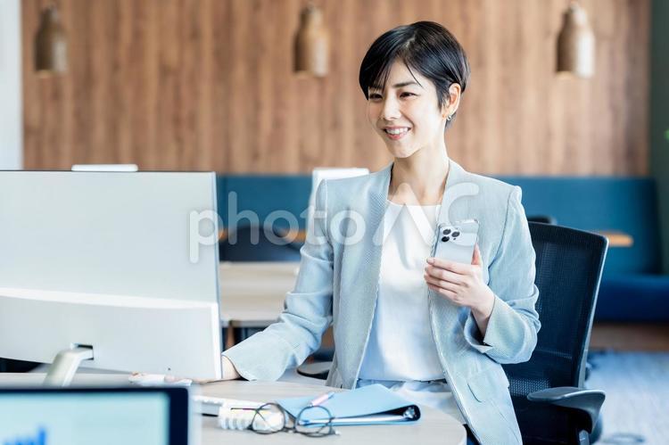 オフィスでスマホを持つビジネスウーマン スマホ,女性,笑顔の写真素材