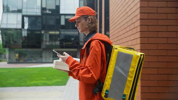 ピザ箱を持ったままスマートフォンを使うフードデリバリーの男性 配達,フードデリバリー,デリバリーの写真素材