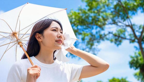 日傘をさして白いハンカチで汗を拭く女性 日傘をさして白いハンカチで汗を拭く女性の写真