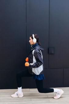 ダンベルを持って足を伸ばす女性 ダンベルを持って足を伸ばす女性 女性,ヘッドフォン,人物の写真素材