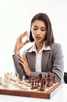 チェスをする女性が駒を持って考えている(白背景) チェスをする女性が駒を持って考えている(白背景)の写真