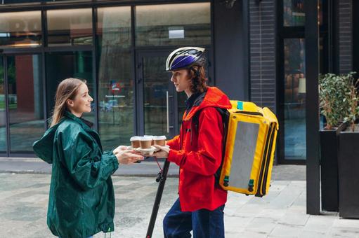 電動キックボードでコーヒーを届けたフードデリバリーの男性と受け取る女性 配達,フードデリバリー,デリバリーの写真素材