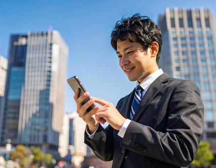 オフィス街でスマホを操作するサラリーマン オフィス街でスマホを操作するサラリーマンの写真