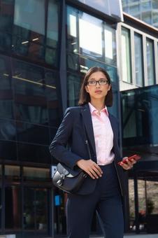 オフィスビルの外でスマートフォンを持って立つアジア人ビジネスウーマン ビジネスウーマン,ビジネス,女性の写真素材