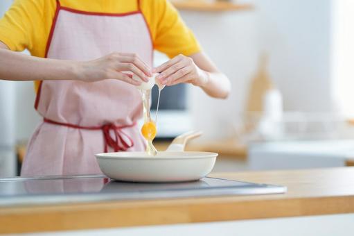 フライパンの上で卵を割る手元の写真