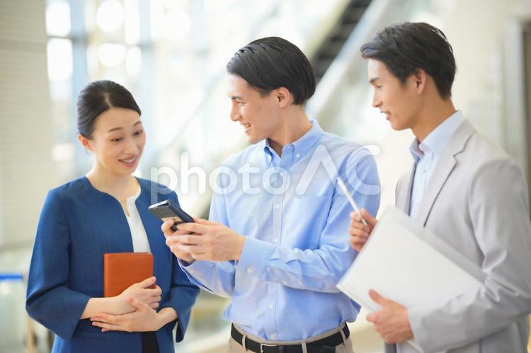 スマホを見ながら話をする3人のオフィスワーカー ビジネスマン,ビジネスウーマン,会社員の写真素材