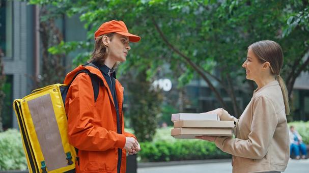 屋外でピザのデリバリーを受け取る女性と配達員の男性の写真