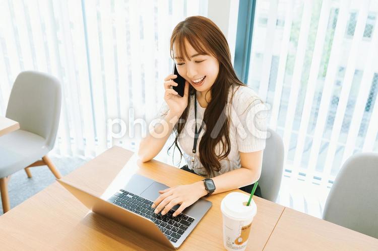 スマホで話しながらパソコンを使う女性 女性,パソコン,スマホの写真素材