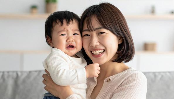泣いている赤ちゃんを抱っこする笑顔の母親 泣いている赤ちゃんを抱っこする笑顔の母親の写真